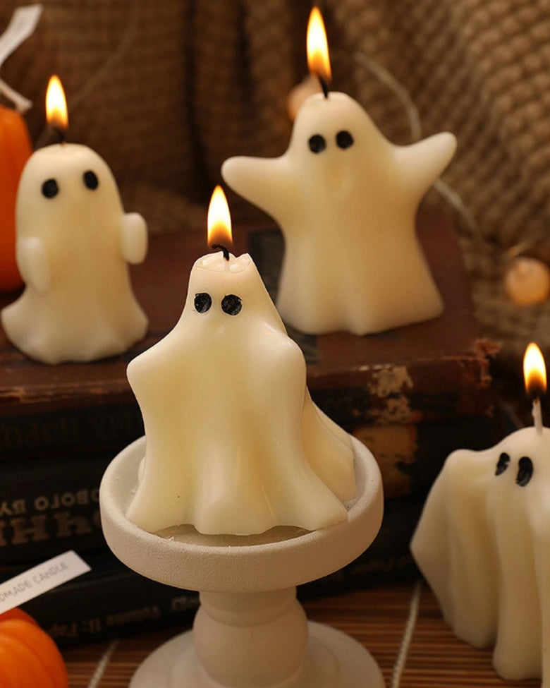 Lit white ghost-shaped candles arranged on a wooden display, including one on a pedestal.