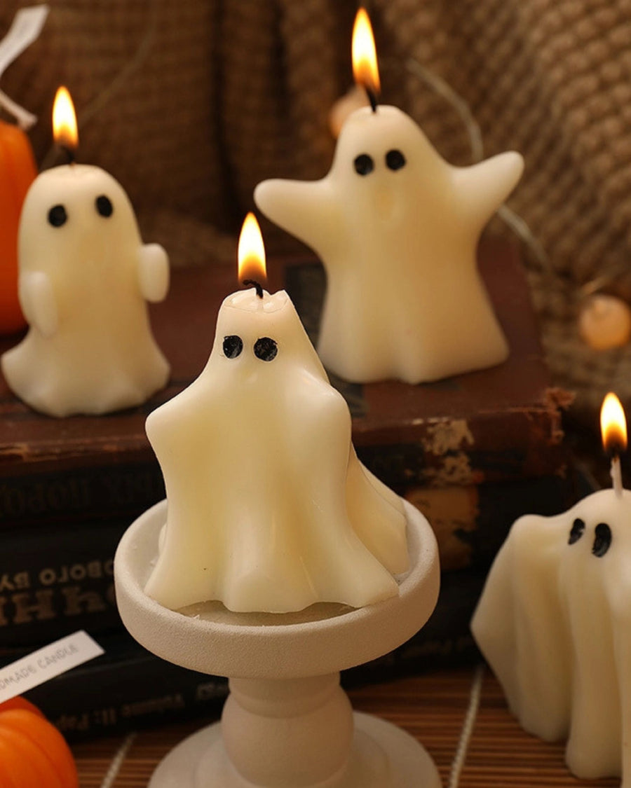 Lit white ghost-shaped candles arranged on a wooden display, including one on a pedestal.