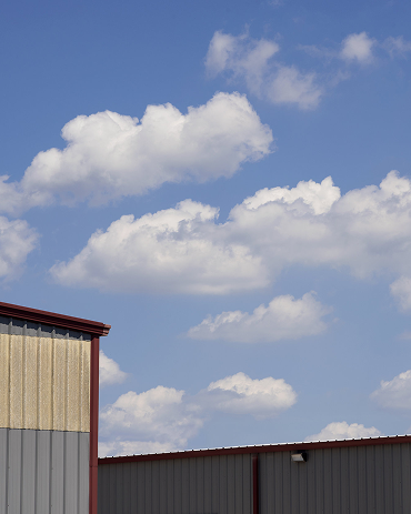 Blue sky with white clouds above the roofs of two industrial-style buildings