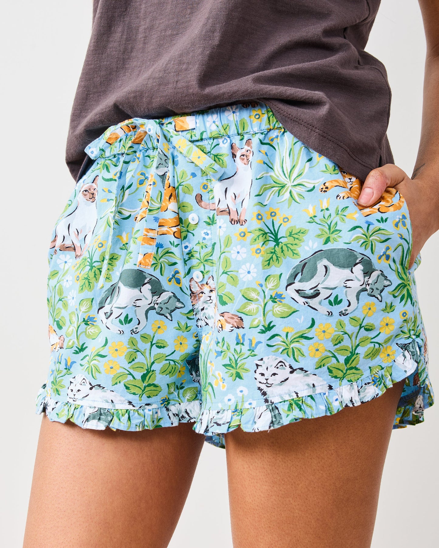 Close front view of blue cat-print shorts with drawstring waist, buttons, pockets, and ruffled hems